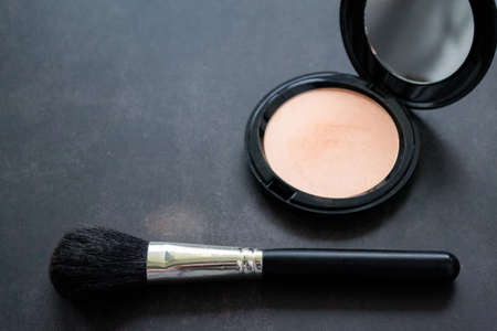 A black makeup brush next to an open box with a mirror and powder puff and pink powder. Black background. Copy space.の写真素材