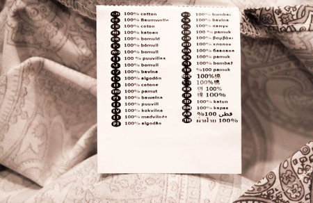White laundry label tag with sign cotton in 36 languages on bed linen.