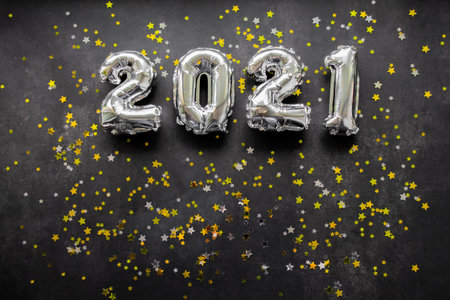 Inflatable numbers New Year 2021 on black background with shiny golden and silver stars. Copy space.
