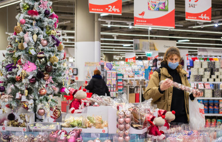 Moscow, Russia, November 2020: a young masked woman looks at and selects Christmas toys at a Christmas sale in a shopping Mall.のeditorial素材