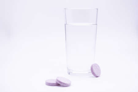 A glass of clean water next to pink tabletsの写真素材