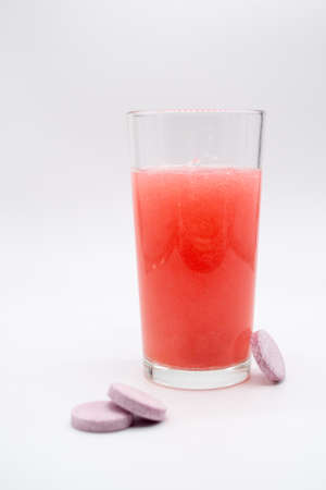 In a glass with pink red water next to pink tabletsの写真素材