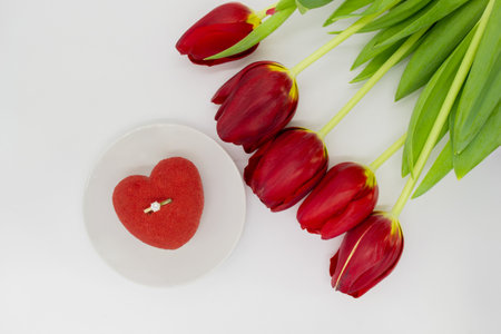 A bouquet of red tulips with a heart-shaped cake and gold ring with a diamond.の写真素材