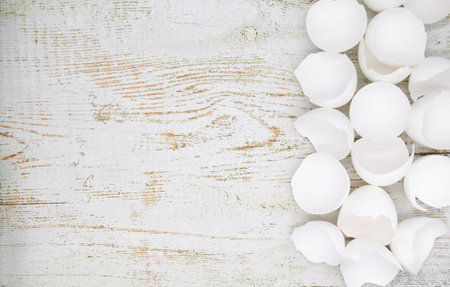Lots of broken white eggshells on an aged wooden background. On the left. Copy space.