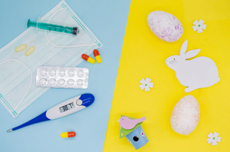 Colorful eggs, decorations, flowers and an Easter Bunny on a yellow background. Medical mask, pills,...