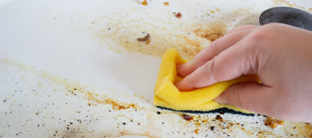 Banner with a hand with a yellow wash sponge washes the very dirty greasy surface of the gas stove. After the sponge, a clean trace remains.の写真素材