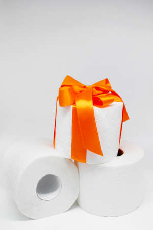 Several rolls of white perforated toilet paper. One roll is tied with a bright orange satin ribbon as a gift.の写真素材