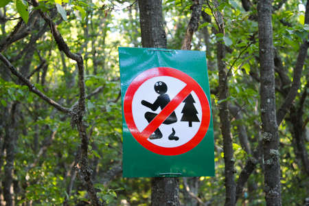 A sign on a tree in a forest or park prohibits people from pooping in nature.の写真素材