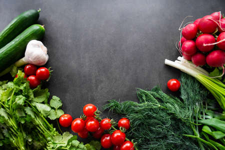 Top view a pile of fresh, ripe vegetables: radishes, tomatoes, cucumbers, herbs, and garlic on a blackboard background. Copy space.の写真素材