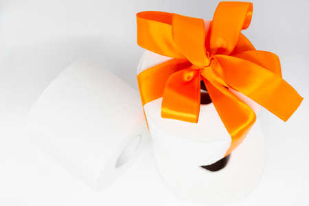 Several rolls of white perforated toilet paper. One roll is tied with a bright orange satin ribbon as a gift.の写真素材