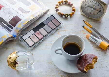 Moscow, Russia, November 2019: Morning routine: unfinished coffee with a piece of chocolate chip cookies, perfume, cosmetics, jewelry. On a blurred background fashion magazine and alarm clock. Flat lay.のeditorial素材