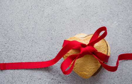 Three heart-shaped cookies: vanilla, chocolate are tied with red ribbon. Gray background, copy...