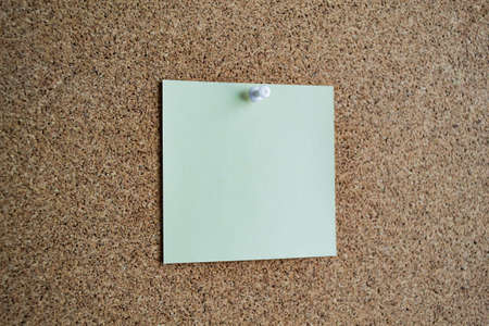 A light green paper note on a cork board, attached with a white pushpin. Copy space.の写真素材