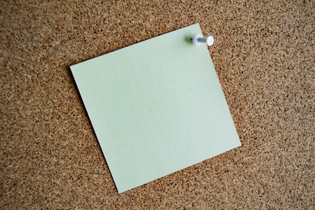 A light green paper note on a cork board, attached with a white pushpin. Copy space.の写真素材