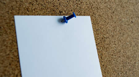 Close-up of a white paper note on a cork board, attached with a blue pushpin. Copy space.の写真素材