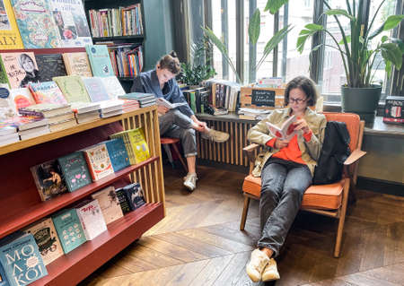St. Petersburg, Russia, August 2021: The interior of modern cozy bookstore in a retro style. Two young hipster girls are sitting, reading.のeditorial素材