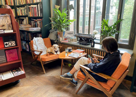 St. Petersburg, Russia, August 2021: Retro style workplace in a bookstore. Young girl with smartphone and fluffy dog sit on armchairs.のeditorial素材