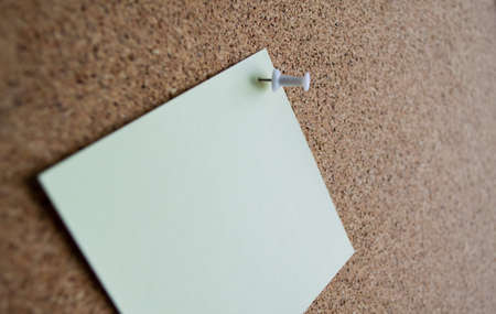 Close up of a pale green paper note on a cork Board, attached with a white pushpin. Copy space.の写真素材