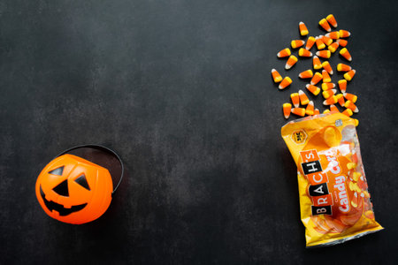 Moscow, Russia, September 2021: Plastic pumpkin basket, candy corn Brachs spilled out of the pack....