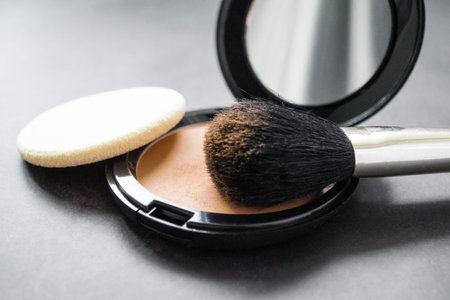 Close-up of a black makeup brush with flesh-colored powder at the end. On the background of an open...