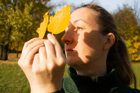 Young woman in profile with yellow leaves, sunlight, shadows, hands close up, autumn inspiration.の写真素材