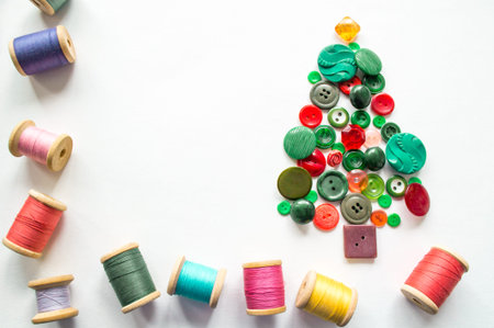 A Christmas tree made of buttons green, red color. Multicolored threads with wooden spools. White...