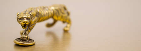 Banner with bronze figure of a tiger with a coin - the symbol of the Chinese new year 2022 on a golden background, copy space. Wishes of good luck, financial well-being and wealth.の写真素材