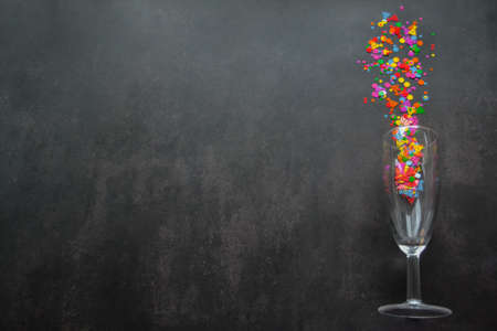 A wine glass with splashes of confetti on dark background. copyspace. Concept of party, celebration, New year, Christmas, birthdayの写真素材