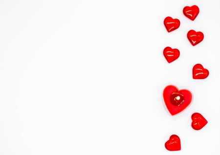 A red burning candle in the shape of a heart and a few glass hearts are lying on a row on the left....