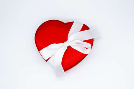 Close up of red satin box in the shape of a heart, tied with a white ribbon on a white background. Concept of love, Valentine's day, gift, surprise.の写真素材
