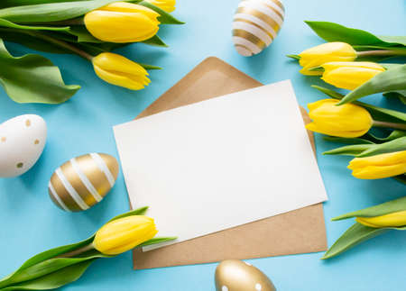 Easter greetings: yellow tulips, golden and white eggs on blue background. A letter with copy space. spring holiday.の写真素材