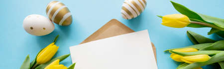 Banner Easter greetings: yellow tulips, golden and white eggs on blue background. A letter with copy space. spring holiday.の写真素材