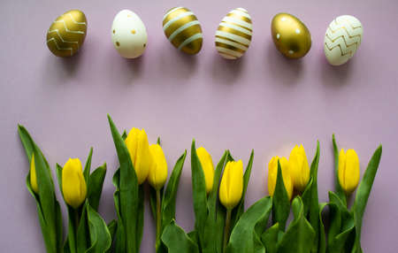 Easter eggs of gold, white color with a pattern and yellow tulips on a purple background. copyspace.の写真素材