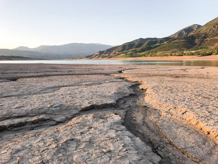 Beautiful landscape with setting sun: mountains, lake, cracked earth with stones -dried-up...