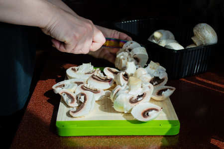 Close-up of hands with sliced fresh mushrooms on a cutting board. Homemade cuisine vegetarian. Sunlight from window, shadows on the table.の写真素材