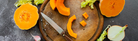 Banner with fresh bright cutted pumpkin on a wooden chopping board with a knife. Celery and garlic, onions and scattered peppercorns and salt.の写真素材