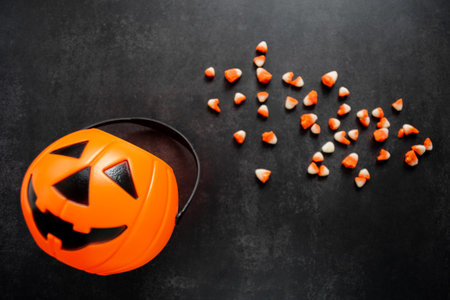 Plastic pumpkin basket with candy corn spilled out. Some of it are broken and look like small teeth. Halloween harmful sweets concept. copyspace.の写真素材
