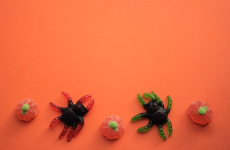 Hallowee: Jelly candies in the form of huge black spiders with green and red legs and pumpkins on orange background. copyspace.の写真素材