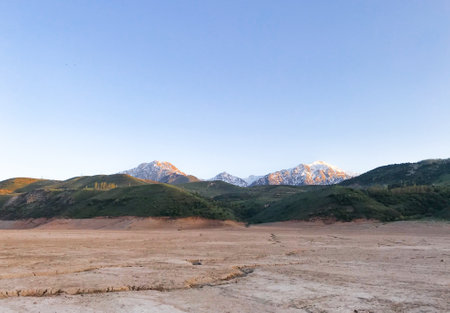 Landscape with mountains, snow peaks and green hills. Dry cracked earth. Drought. The dried-up bottom of the river.の写真素材