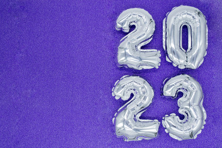 Inflatable shiny silver numbers of the New year 2023 on purple, very peri color background....