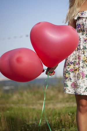 A girl holding two balloons in shape of heartの写真素材