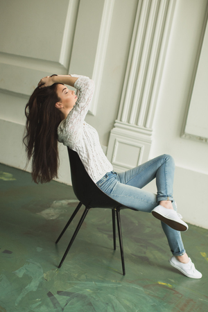 Portrait of young lady sitting on chair in photostudio interiorの写真素材