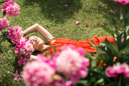 girl lying on green grass under the pink peoniesの写真素材