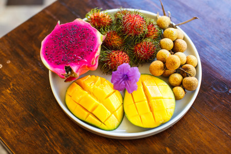 exotic fruits on plate in villa: mango, dragon fruit; mango; pineapple and rambutan