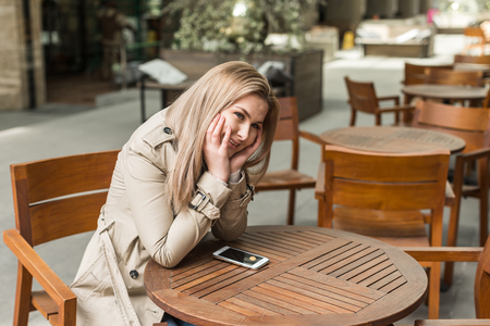 Young girl sitting at  table with a phone in cafeの写真素材