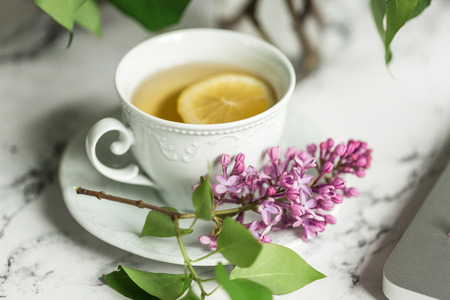 A cup of tea and lilacs next to the laptopの写真素材
