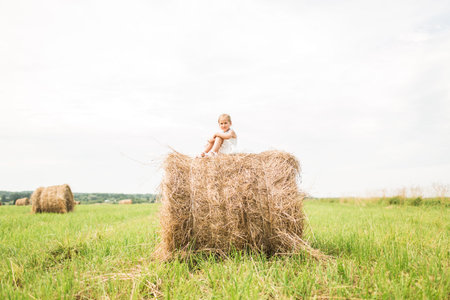 Little girl is sitting on a haystack, a summer concept, a vacationの写真素材