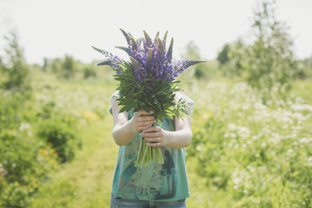 the girl is standing in the field with a bouquet of lupinesの写真素材
