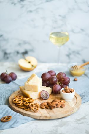 Cheese plate served with grapes, honey, crackers and nuts on a wooden plateの写真素材