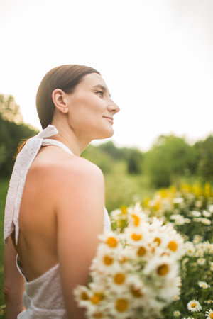 young woman with a large bouquet of daisies sits in natureの写真素材